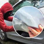 nel cerchio la carrozzeria di un'auto urtata dietro un malvivente prova a forzare una portiera