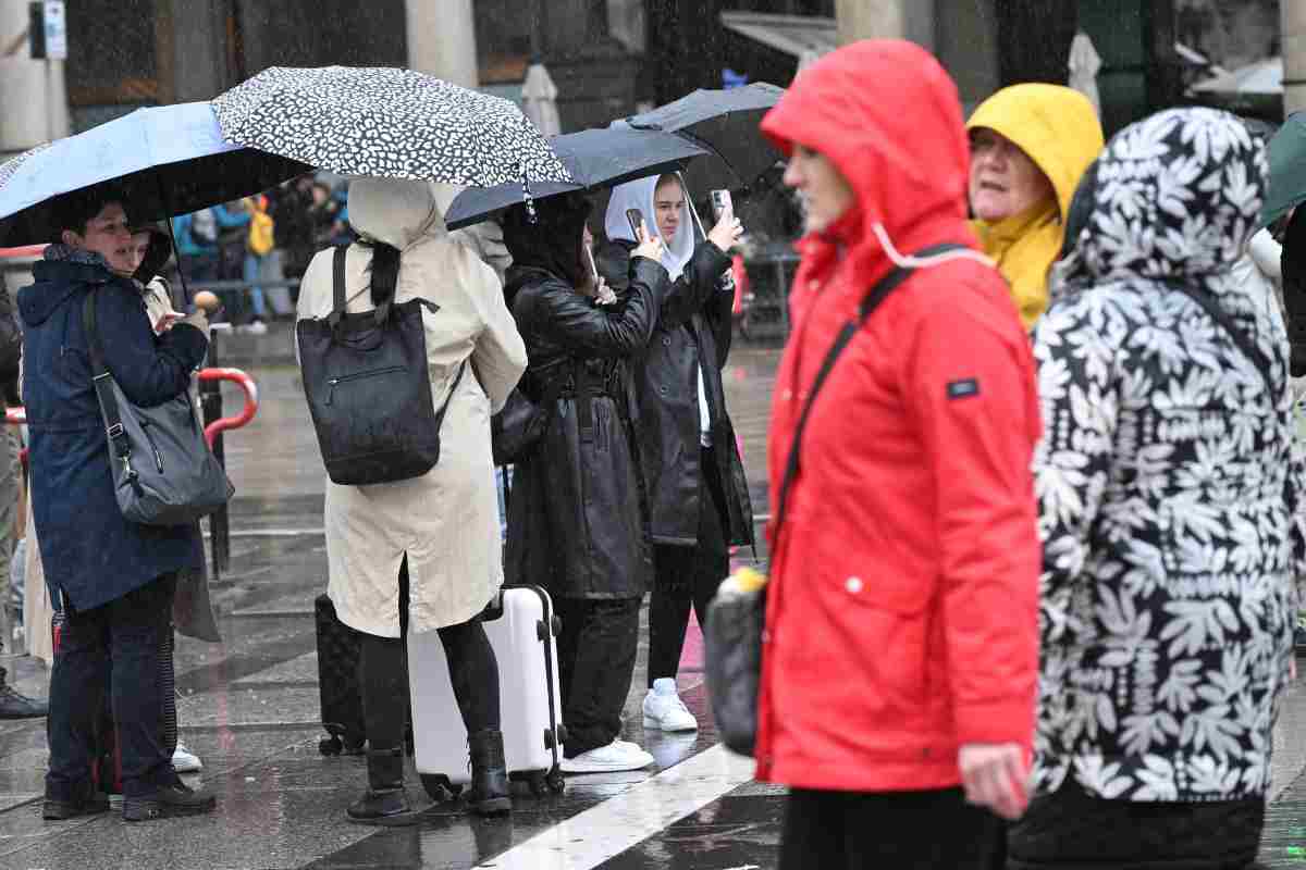 Persone camminano sotto una fitta pioggia in piazza Duomo