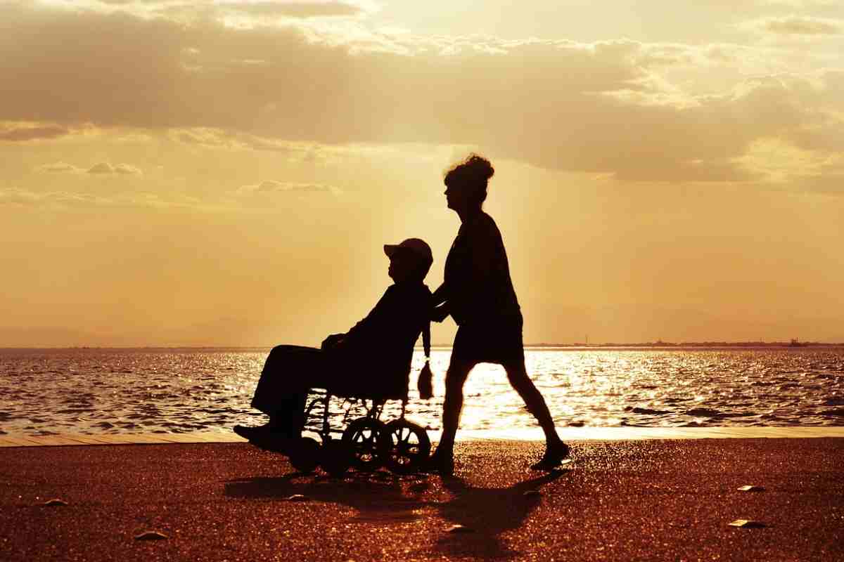 persona che porta una persona con disabilità in giro su spiaggia