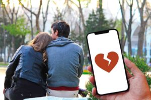 lo schermo di un telefonino con un cuore spezzato e vicino due persone abbracciate