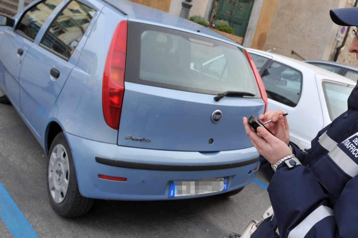 un vigile mentre multa un'auto in sosta