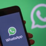 cellulare tra le mani con schermata WhatsApp e logo WhatsApp sullo sfondo