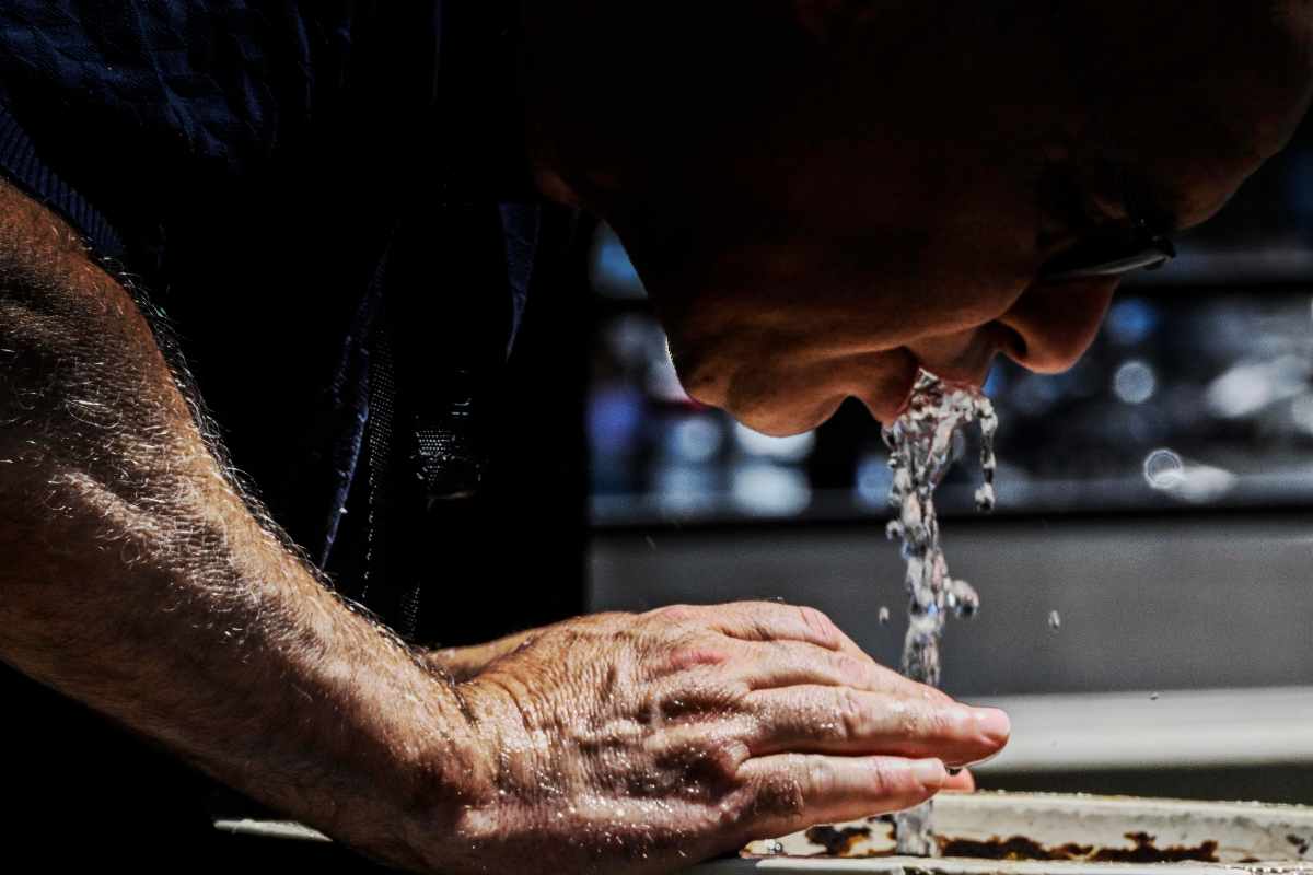 un uomo si disseta con l'acqua di una fontana