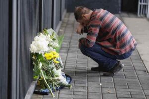 Persona commossa in ginocchio vicino ad un mazzo di fiori