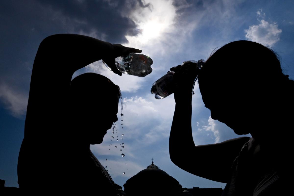 Due persone si bagnano la testa con una bottiglina d'acqua