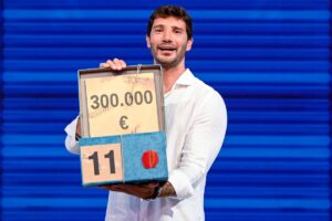 Stefano De Martino in primo piano col pacco da 300.000€ di "Affari Tuoi"