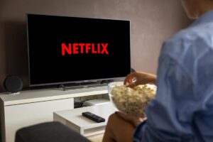Uomo con popcorn sul divano davanti al televisore con Netflix