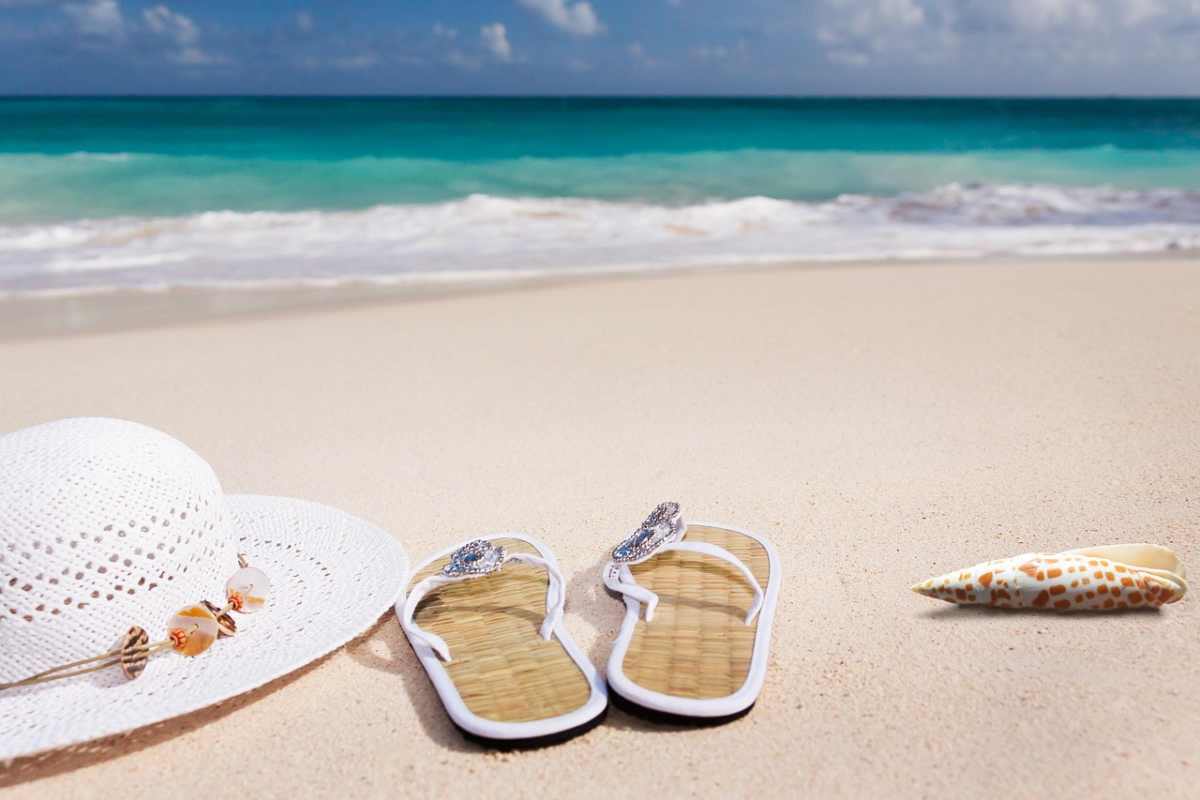 ciabatte e cappello sulla sabbia con il mare sullo sfondo