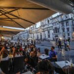 Persone sedute ai tavoli esterni di un bar sotto un gazebo