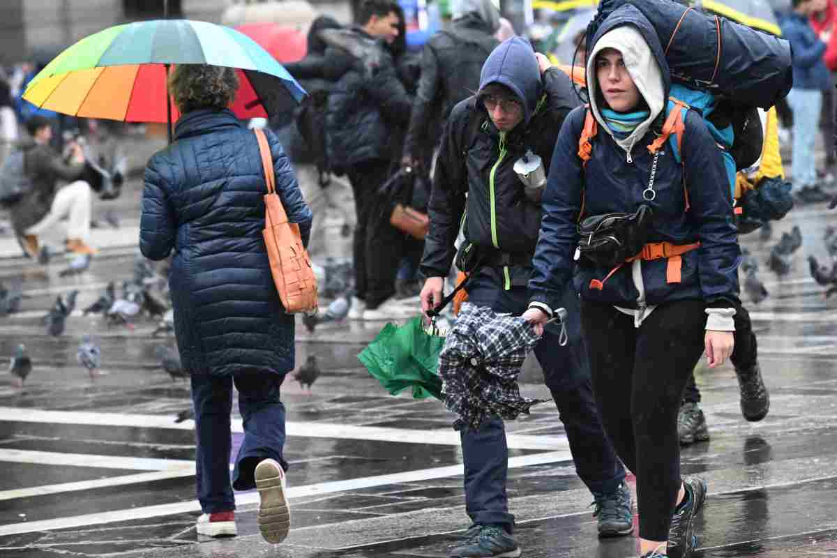 Persone che camminano con giubbini ed ombrelli aperti per ripararsi dalla pioggia