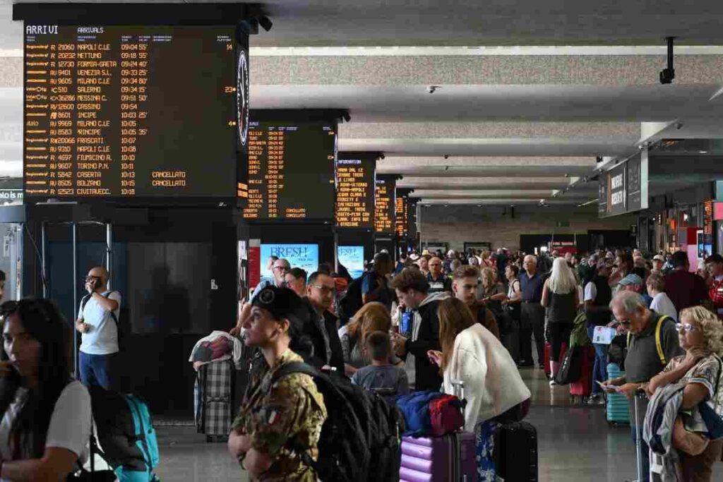 Persone che passeggiano in stazione osservando i monitor di servizio