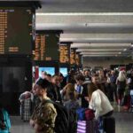 Persone che passeggiano in stazione osservando i monitor di servizio