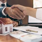due mani che si stringono e sotto un modellino di una casa
