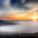 sole che spunta in una vallata coperta da nebbia